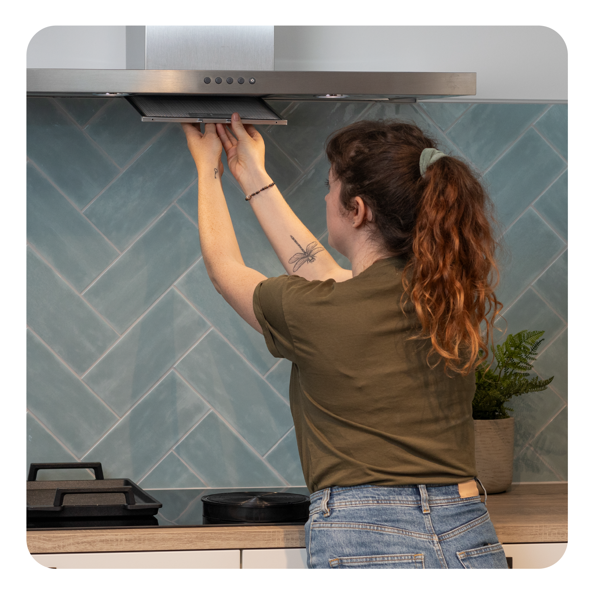 Eine Frau ersetzt einen Luftfilter. Sie steht vor einer blau gefliesten Wand und einer Küchenhaube.