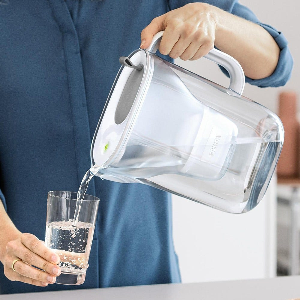 Una persona versa acqua da una caraffa in un bicchiere. La caraffa contiene un filtro per l'acqua.