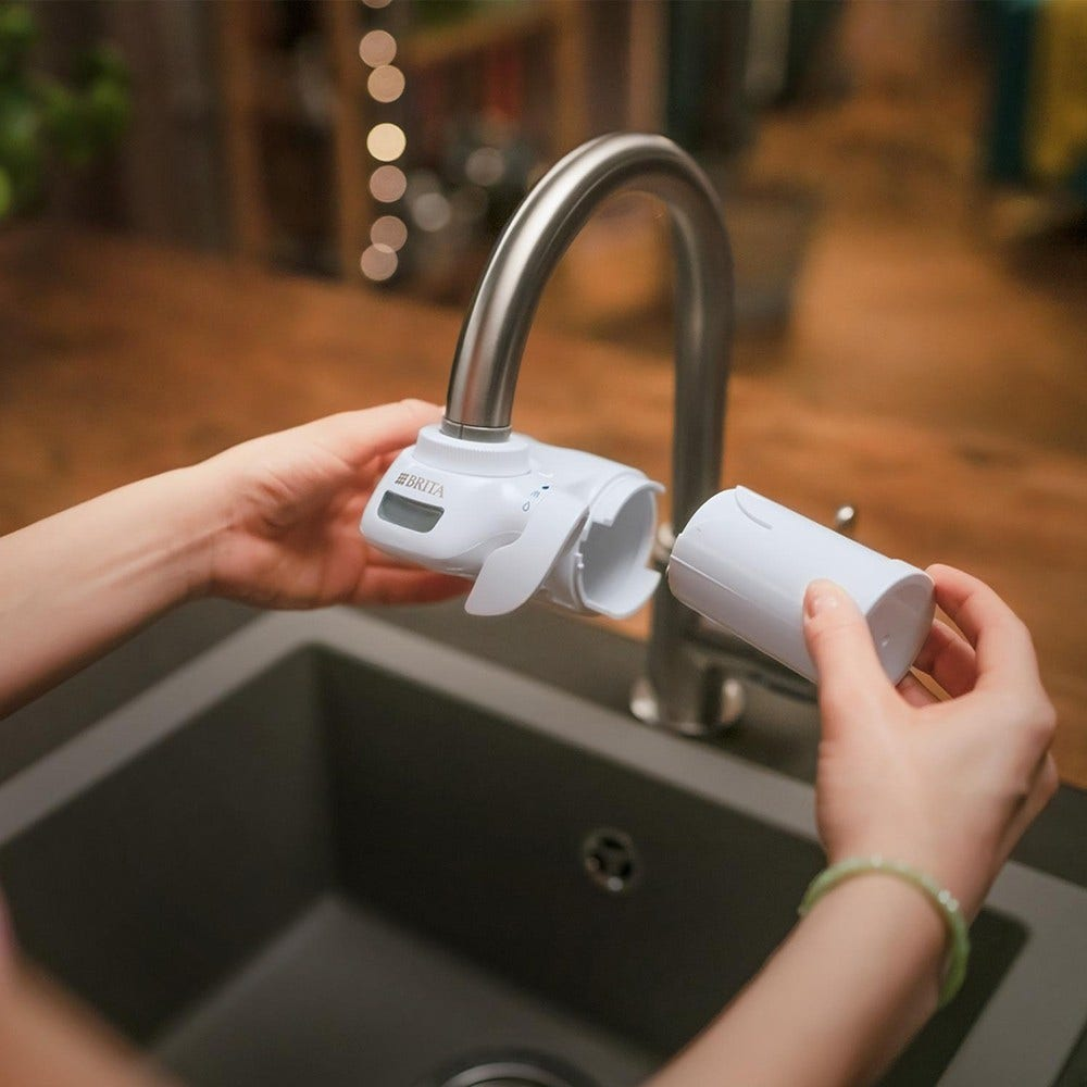 Hände montieren ein Wasserfiltersystem an einem Küchenwasserhahn. Ein weißer Filter wird am Wasserhahn befestigt.