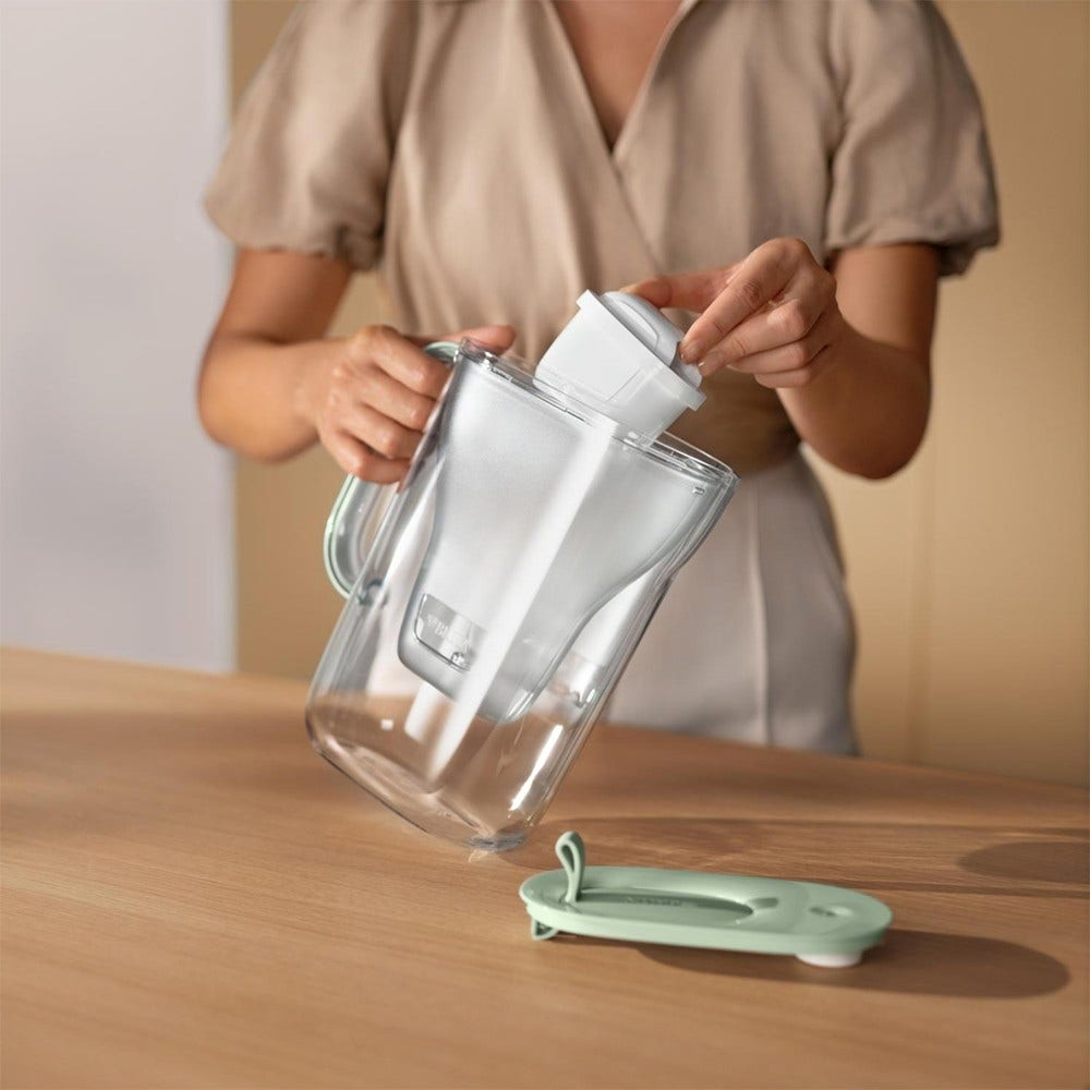 Eine Person, die einen weißen Wasserfilter in eine transparente Kanne mit blauem Deckel einsetzt.