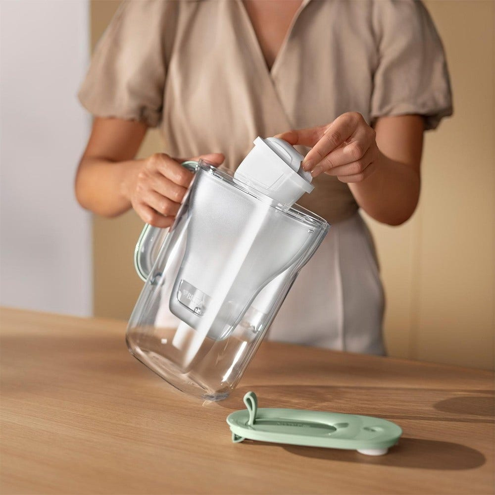 Eine Person setzt eine Wasserfilterkartusche in einen Wasserfilterkrug ein, der Deckel liegt daneben.