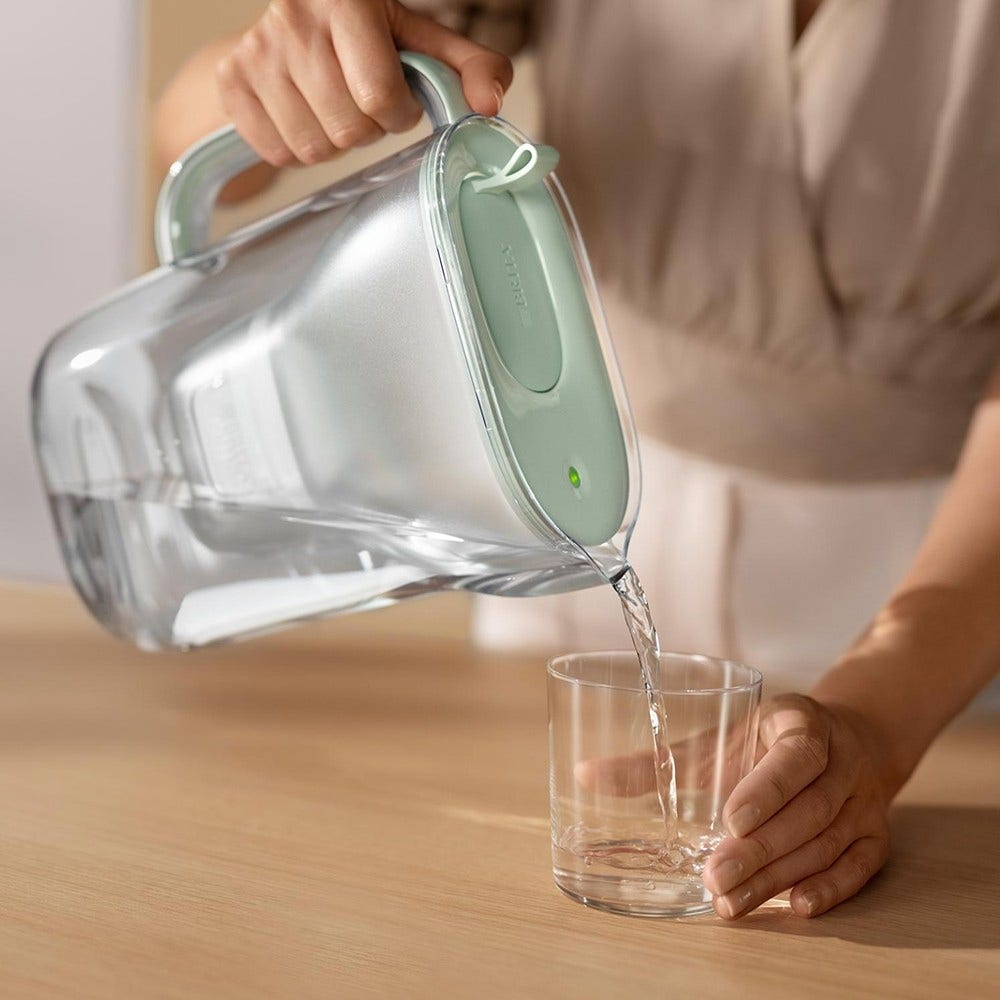 Eine Person gießt Wasser aus einem Wasserfilterkrug in ein Glas. Das Wasser ist klar.