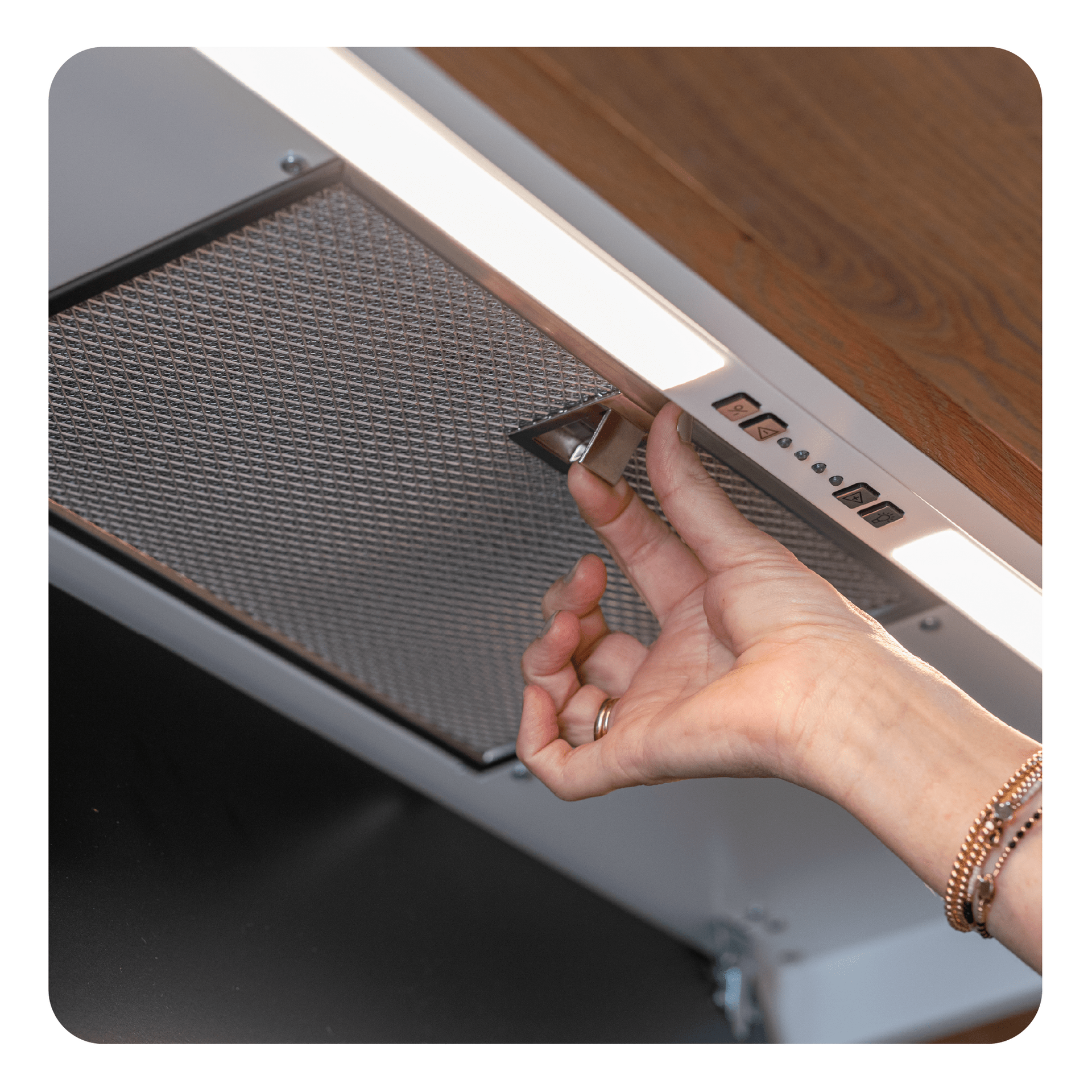 Dłoń sięgająca do okapu kuchennego. Okap jest srebrny z światłami i kontrolkami, obok drewnianych szafek.