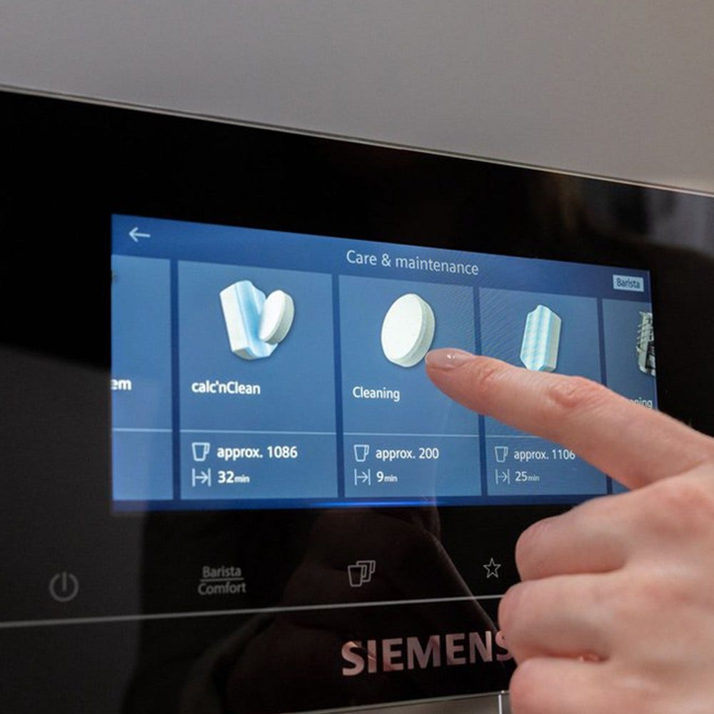 Ręka wskazująca ikonę czyszczenia na cyfrowym ekranie ekspresu do kawy.