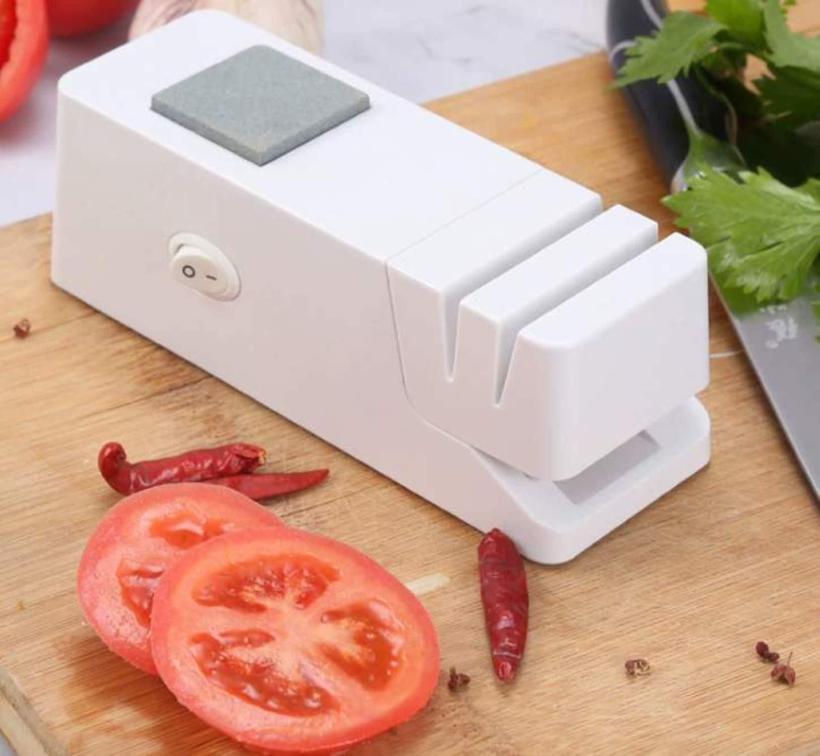 Ein weißer Messerschärfer mit Tomatenscheiben, roten Chilis und einem Messer auf einem Holzbrett.