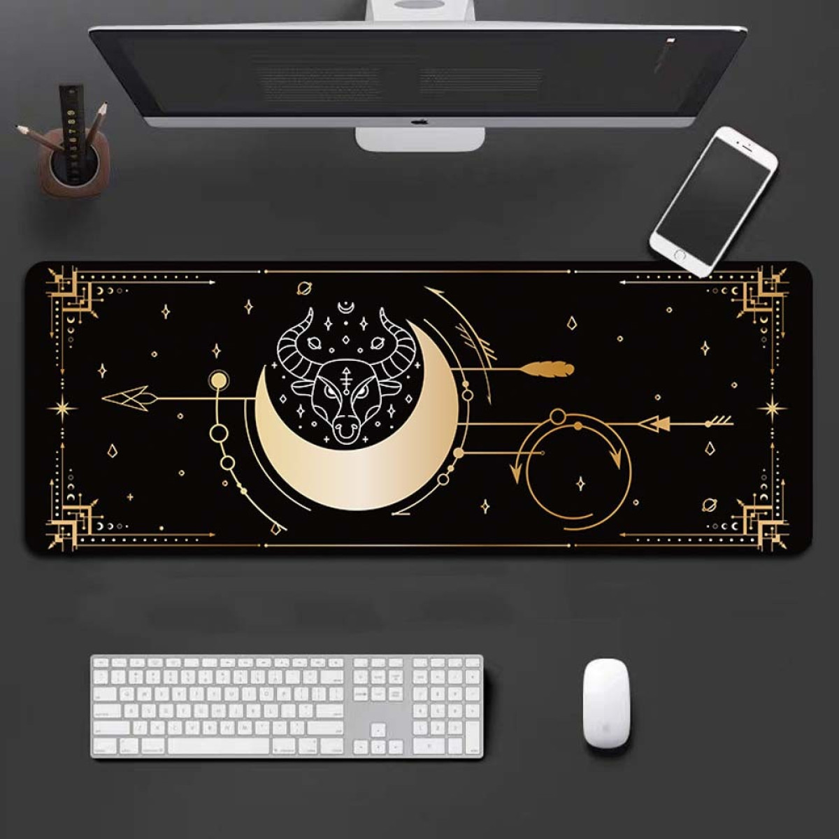 Black desk mat with golden celestial design featuring a bull and moon. Keyboard, mouse, phone, monitor.