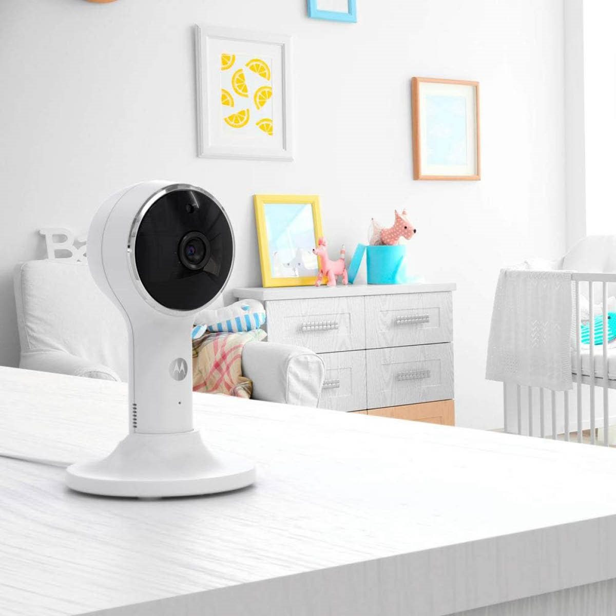 Caméra de moniteur pour bébé blanche sur une surface blanche dans une pièce. L'arrière-plan comprend une décoration et un berceau.