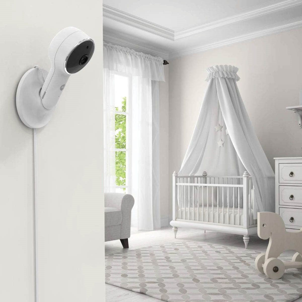 Caméra de babyphone blanche montée sur un mur dans une chambre d'enfant. Un berceau est à l'arrière-plan.
