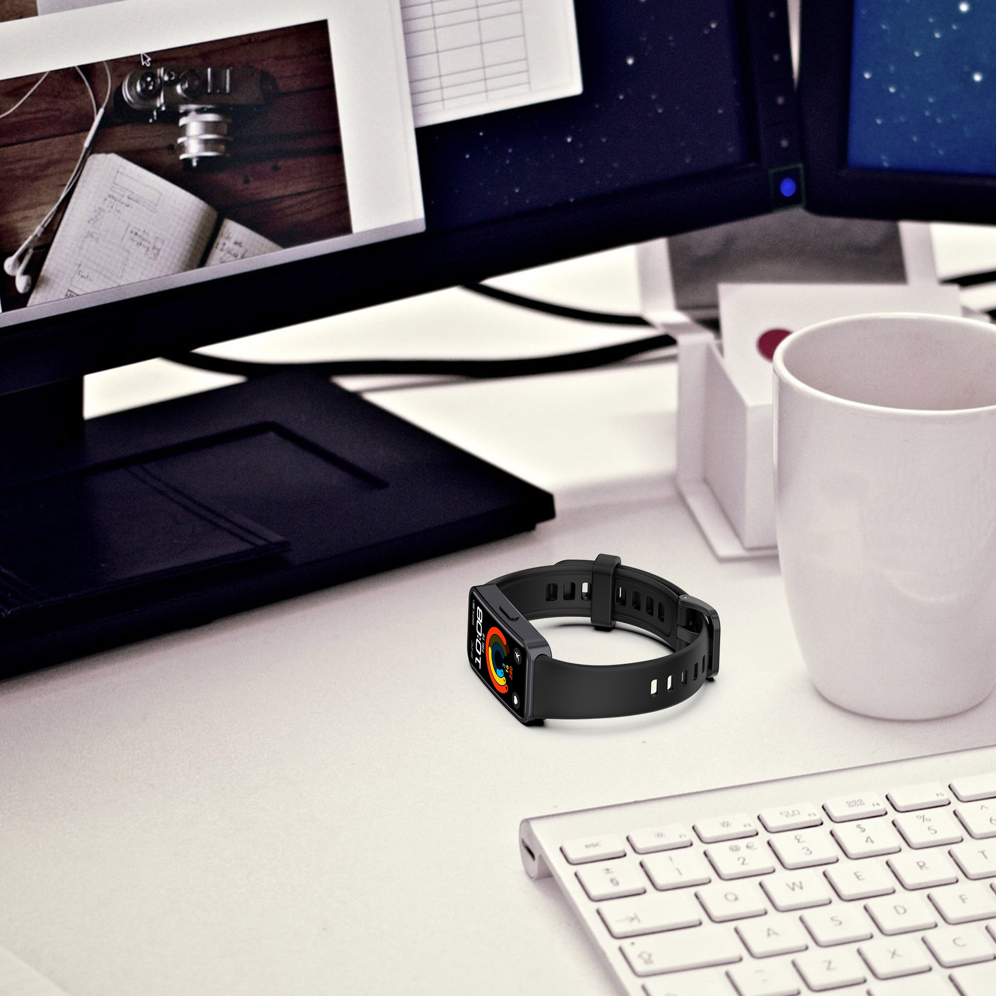 Smartwatch leżący na białym biurku z klawiaturą i monitorami komputerowymi w tle.