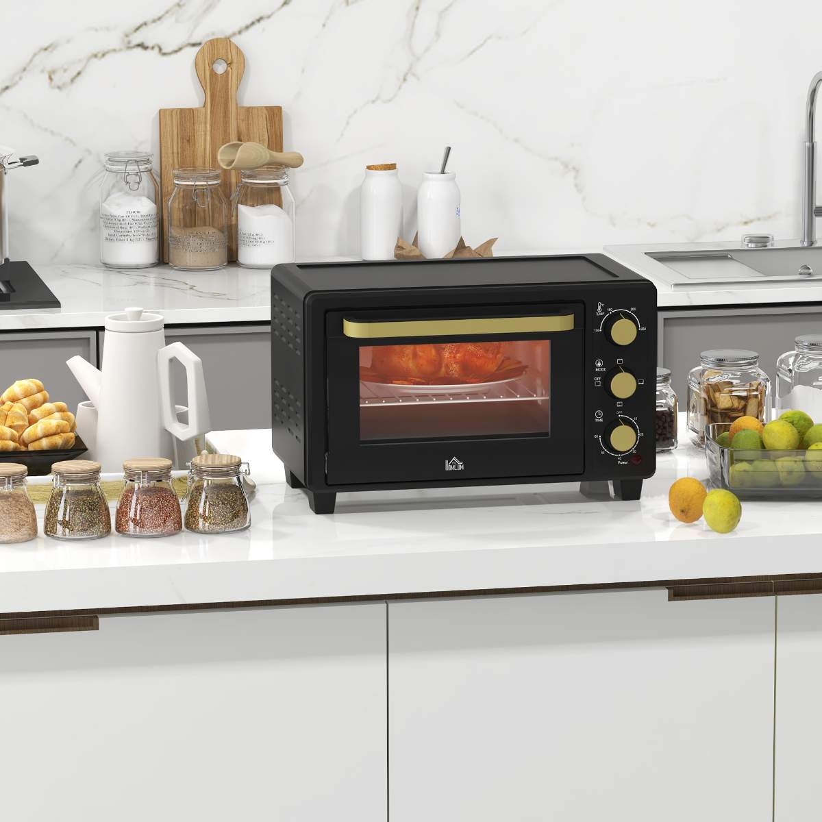 Ein schwarzer Mini-Backofen steht auf einer weißen Theke mit Lebensmitteln und Küchenutensilien drumherum.