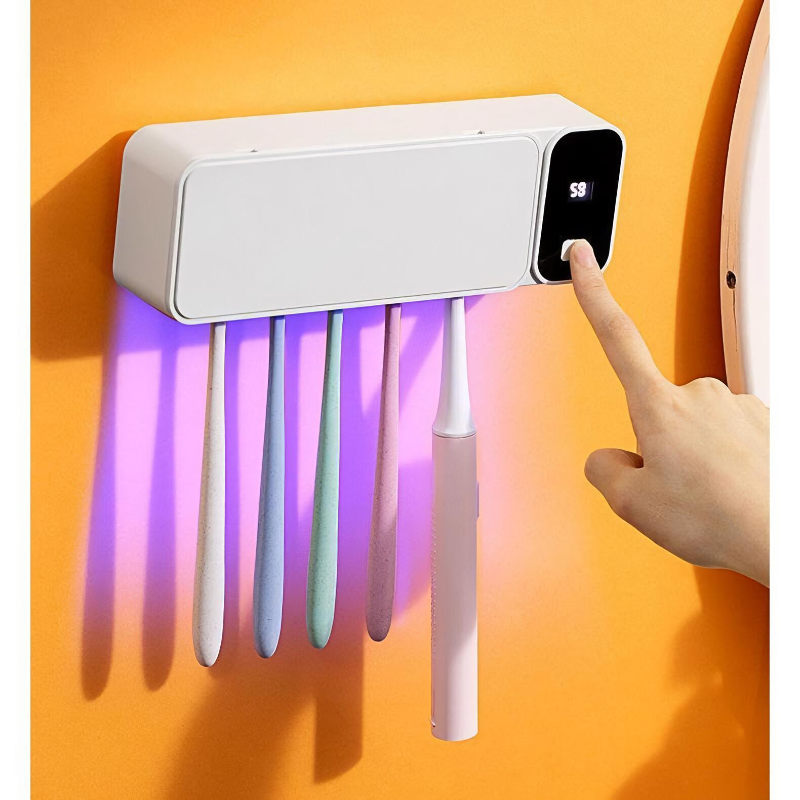 Ein an der Wand befestigter Zahnbürstenhalter mit fünf Zahnbürsten und einem Digitaldisplay. Eine Hand berührt das Display.