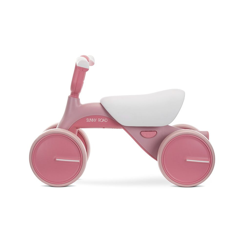 Bicicleta de equilibrio rosa. La bicicleta tiene un asiento blanco y ruedas rosas. El manillar es curvo.