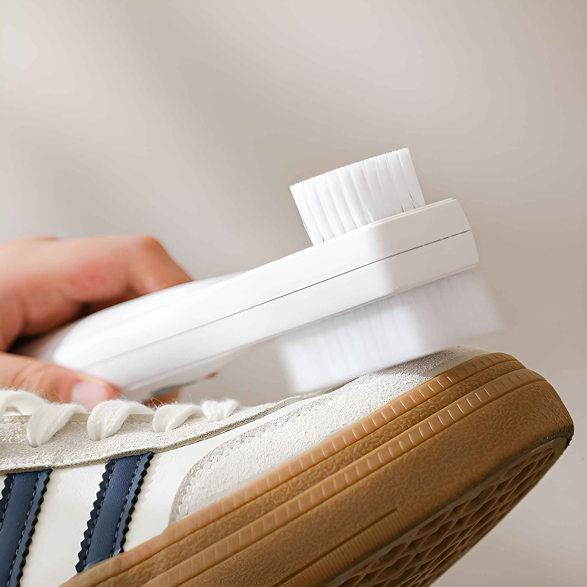 Eine Hand reinigt mit einer weißen Bürste einen weißen und blauen Turnschuh. Die Bürste ist weiß.