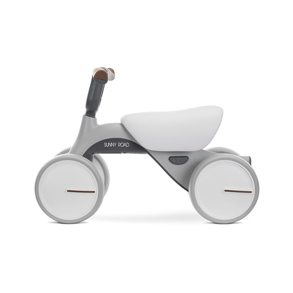 Bicicleta para bebé gris y blanca. Tiene cuatro ruedas y un asiento.