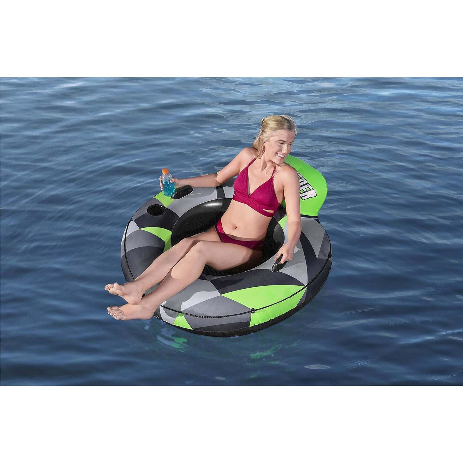 Eine Frau in rotem Bikini sitzt auf einem Schneerohr im Wasser. Sie hält eine Flasche und lächelt.
