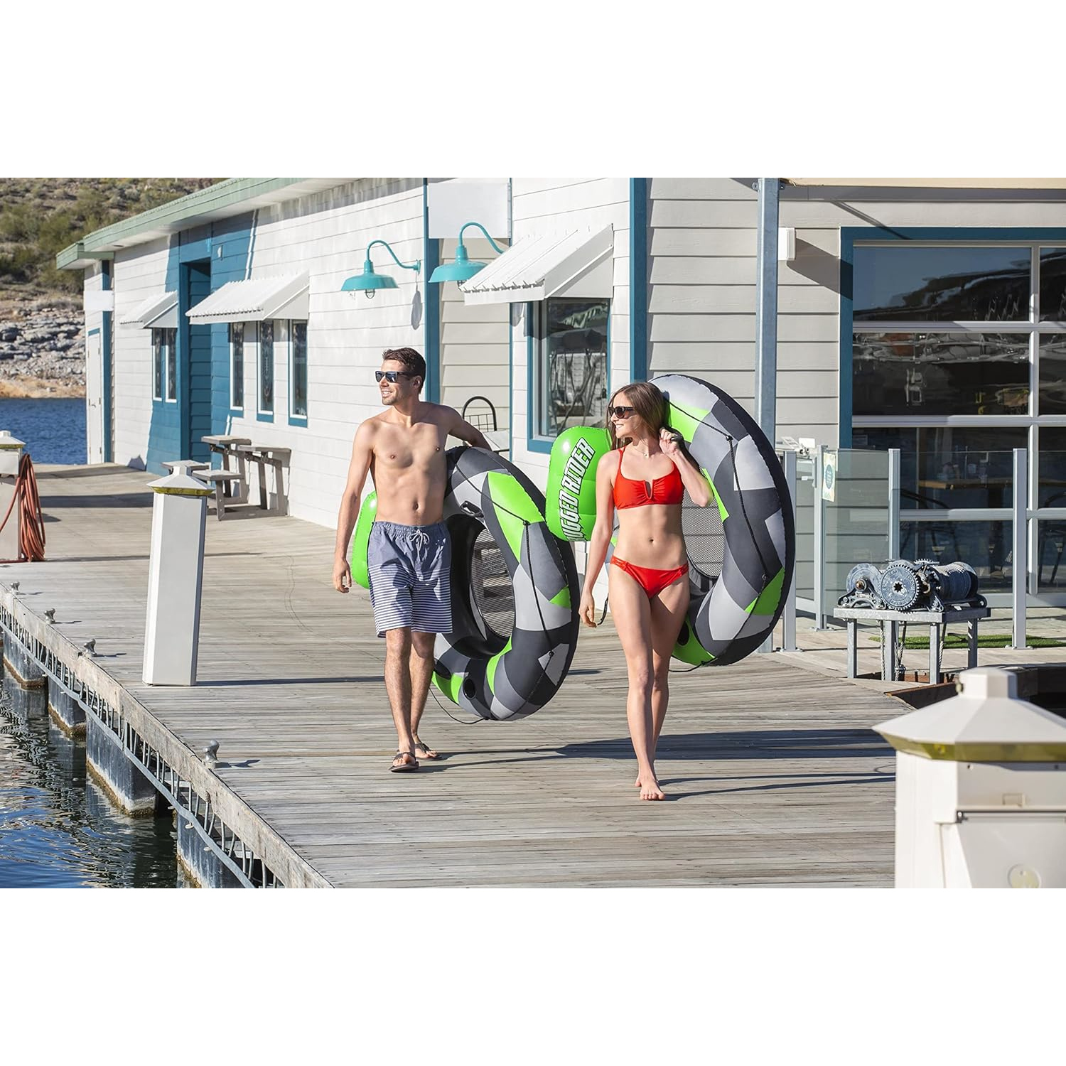 Ein Mann und eine Frau gehen auf einem Steg, jeder trägt eine Schwimmreifen.