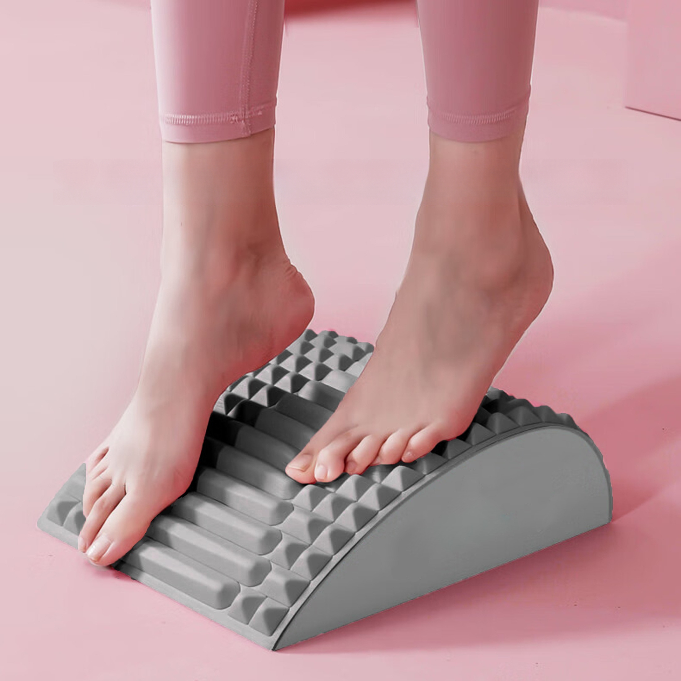 Füße auf einem grauen, gewölbten Massagegerät. Die Füße einer Person befinden sich oben auf dem Gerät, rosa Hintergrund.