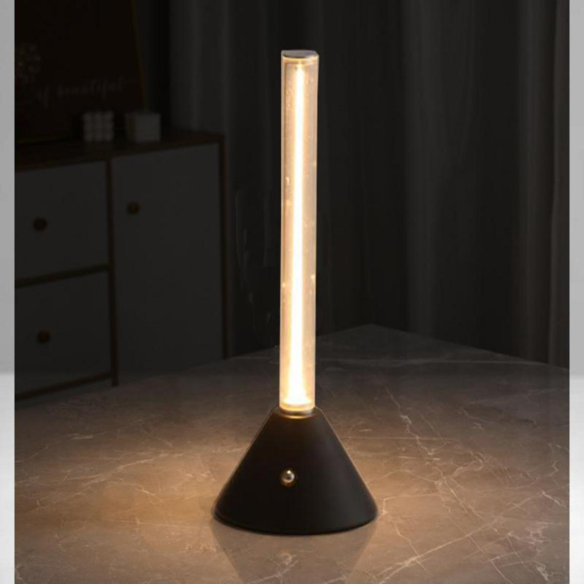Eine Tischlampe mit schwarzem Sockel und leuchtendem Rohr, auf marmorähnlicher Oberfläche.
