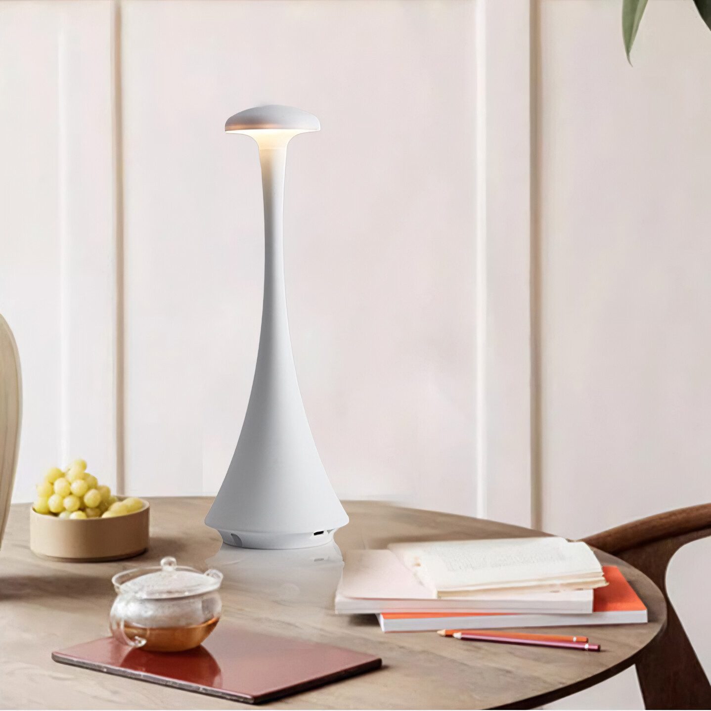 Weiße Lampe auf einem Tisch. Bücher, eine Schale mit Trauben und eine Teekanne stehen ebenfalls auf dem Tisch. Weißer Hintergrund.