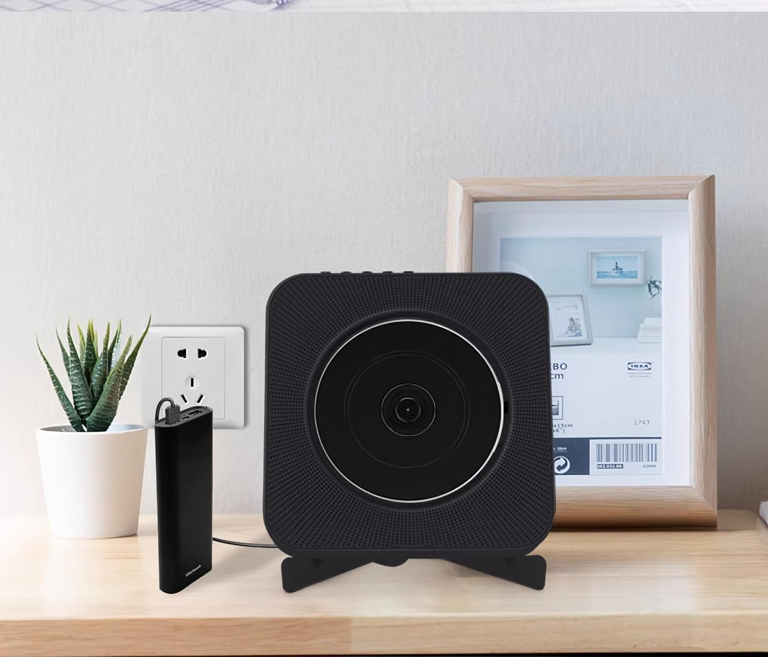 CD-Player auf Ständer, Powerbank an Steckdose angeschlossen, gerahmtes Bild, Topfpflanze.