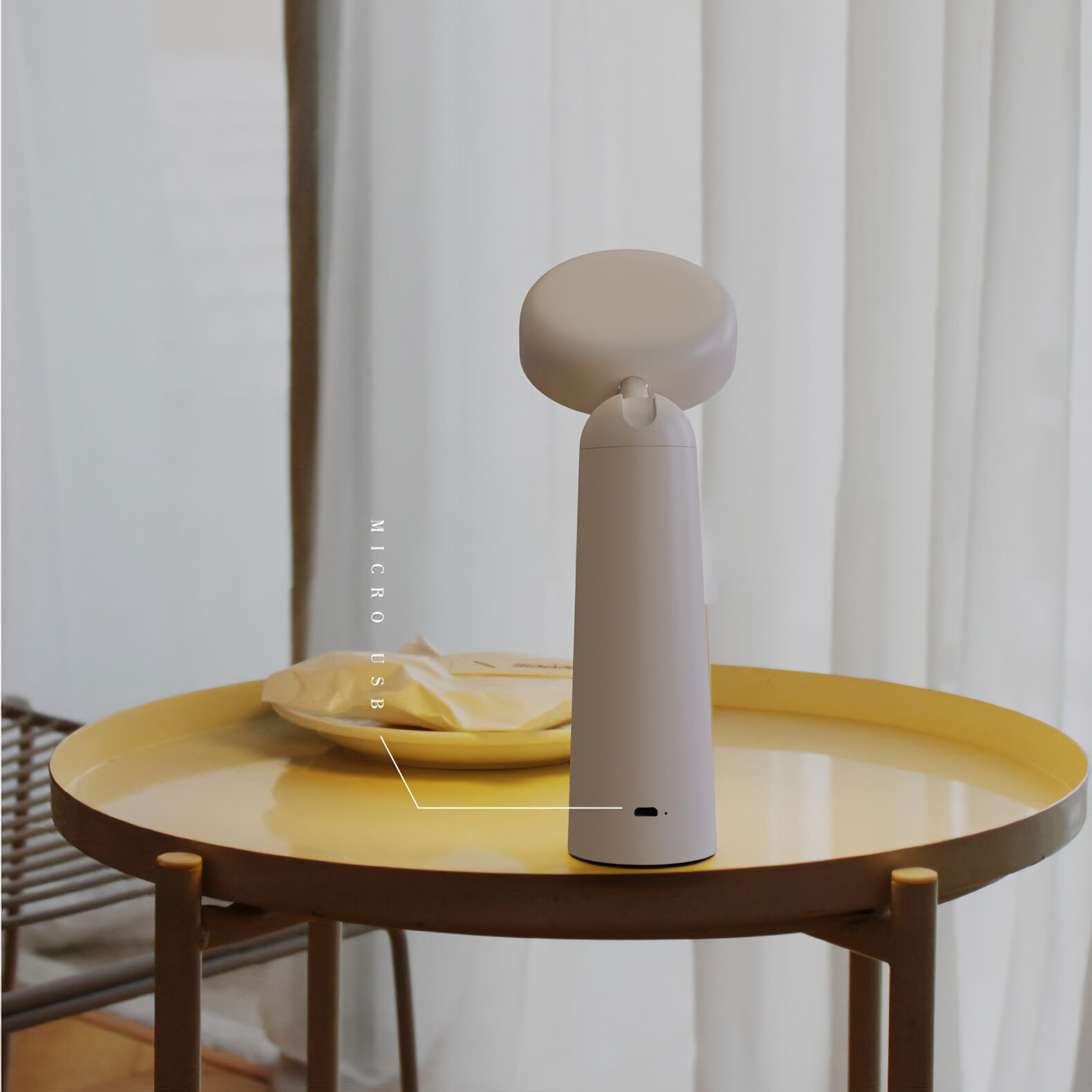Weiße Lampe mit rundem Oberteil auf einem gelben Tisch. Daneben ein Teller mit Papier.