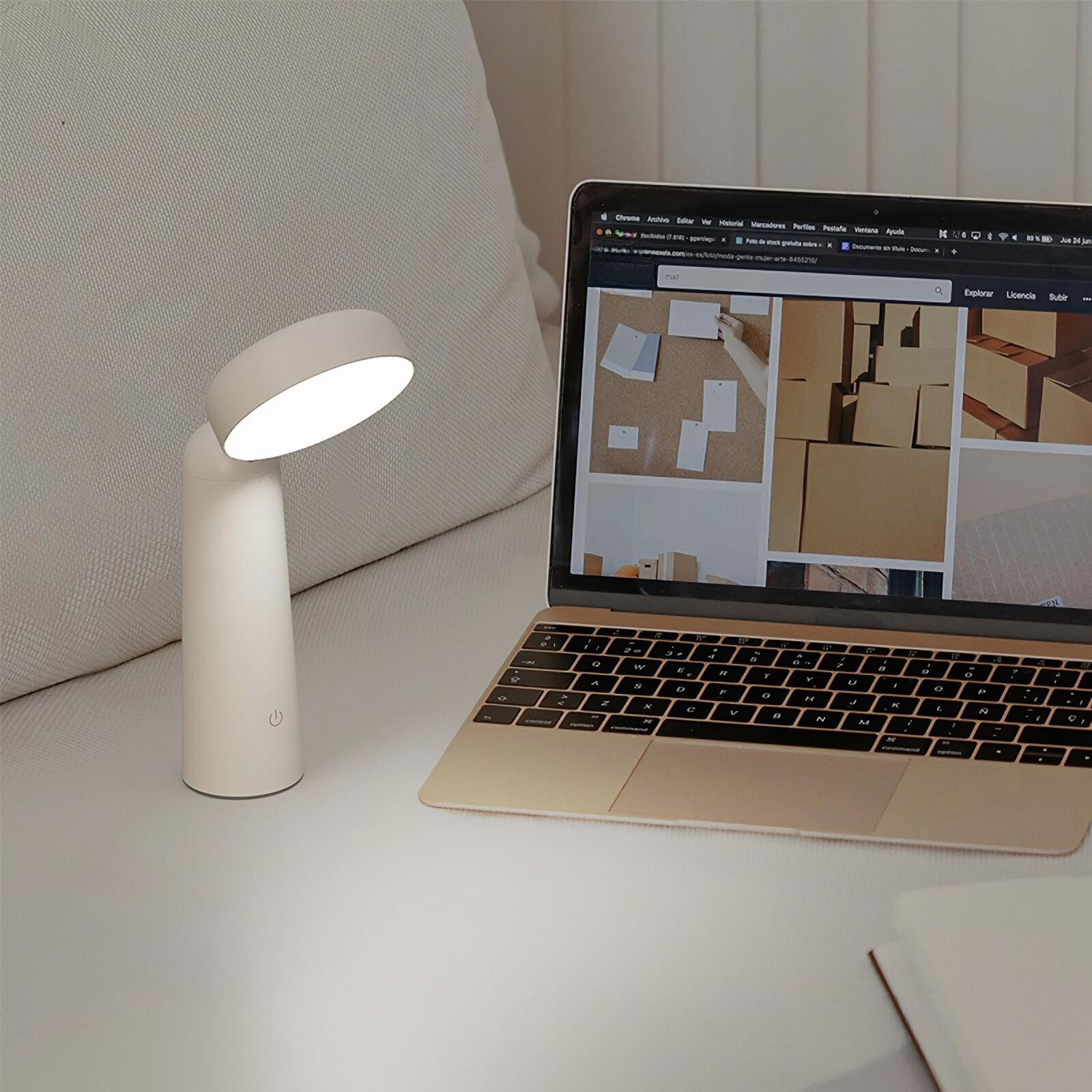 Eine weiße Schreibtischlampe und ein Laptop auf einer Oberfläche. Die Lampe ist auf den Laptop gerichtet.
