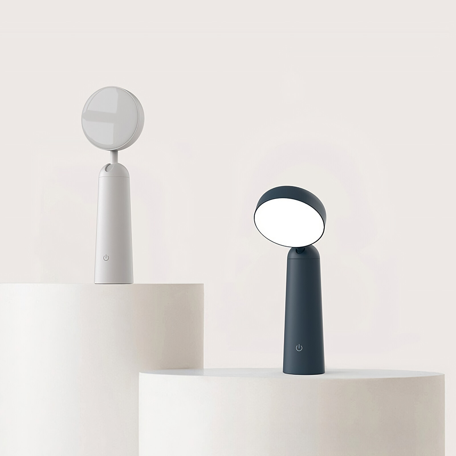 Zwei Lampen auf Oberflächen. Eine weiß, die andere schwarz. Beide haben zylindrischen Sockel und rundes Licht.