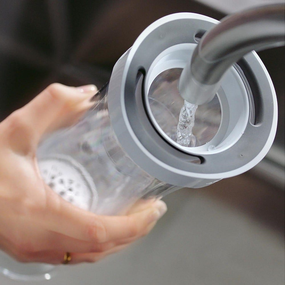 Eine Hand hält einen klaren Wasserfilter, der mit Leitungswasser gefüllt wird.