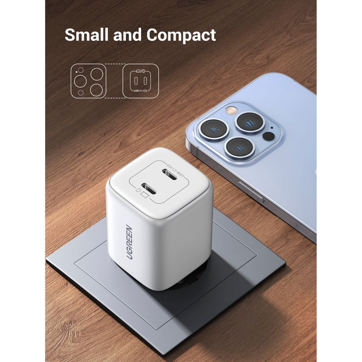 Cargador UGREEN blanco con dos puertos, junto a un teléfono sobre una superficie de madera, con toma de corriente.