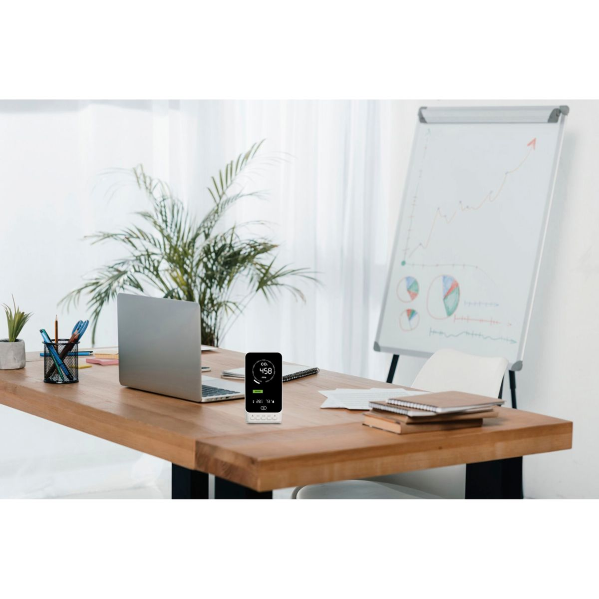 Ein Schreibtisch mit Laptop, kleinem Bildschirm, Stiften und einer Tafel im Hintergrund.