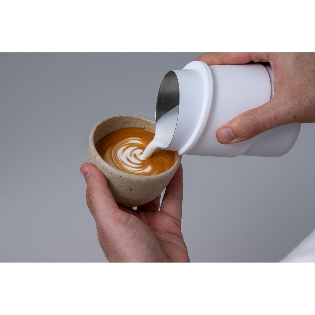 Eine Person gießt Milch aus einem Krug in eine Tasse Kaffee und kreiert Latte Art.