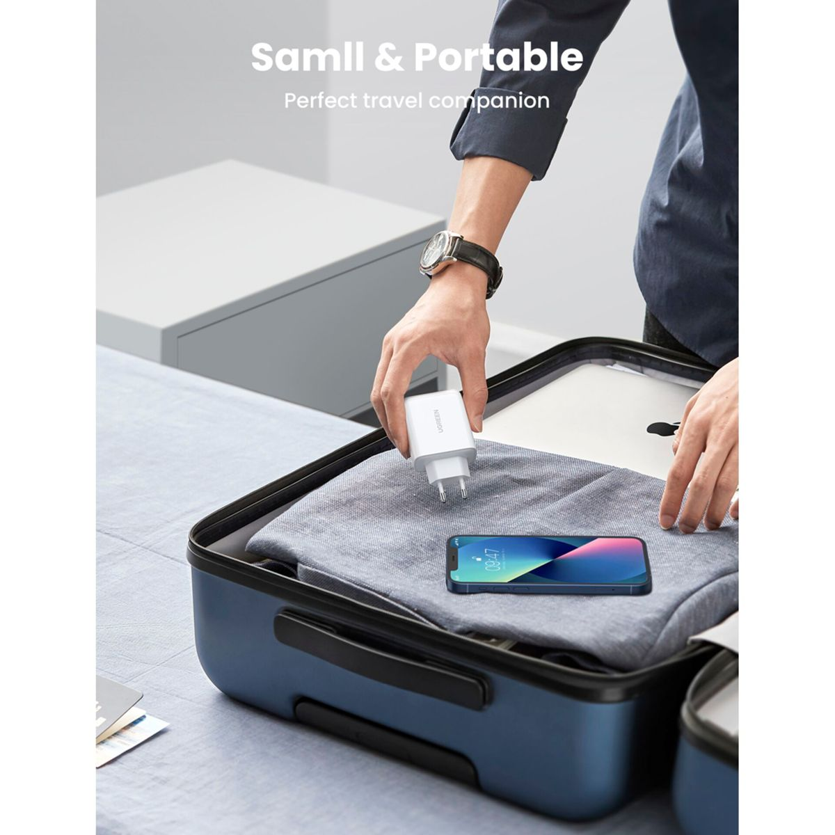 Osoba pakuje białą ładowarkę obok telefonu w niebieskiej walizce. Ładowarka jest marki UGREEN.