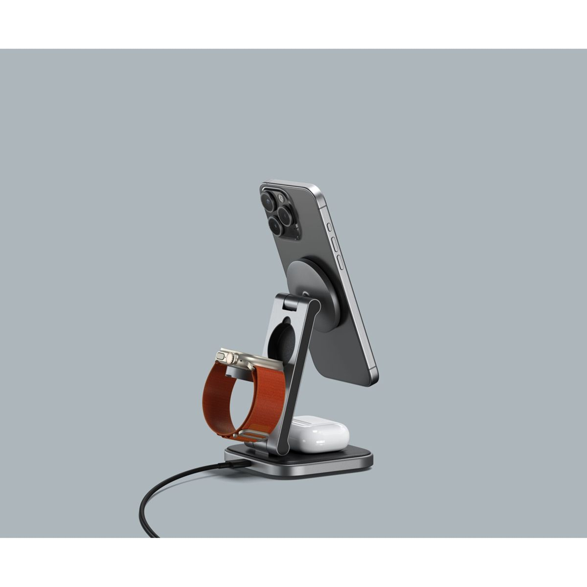 Un supporto di ricarica tiene un telefono, un Apple Watch e AirPods su sfondo grigio. Il supporto è argentato.