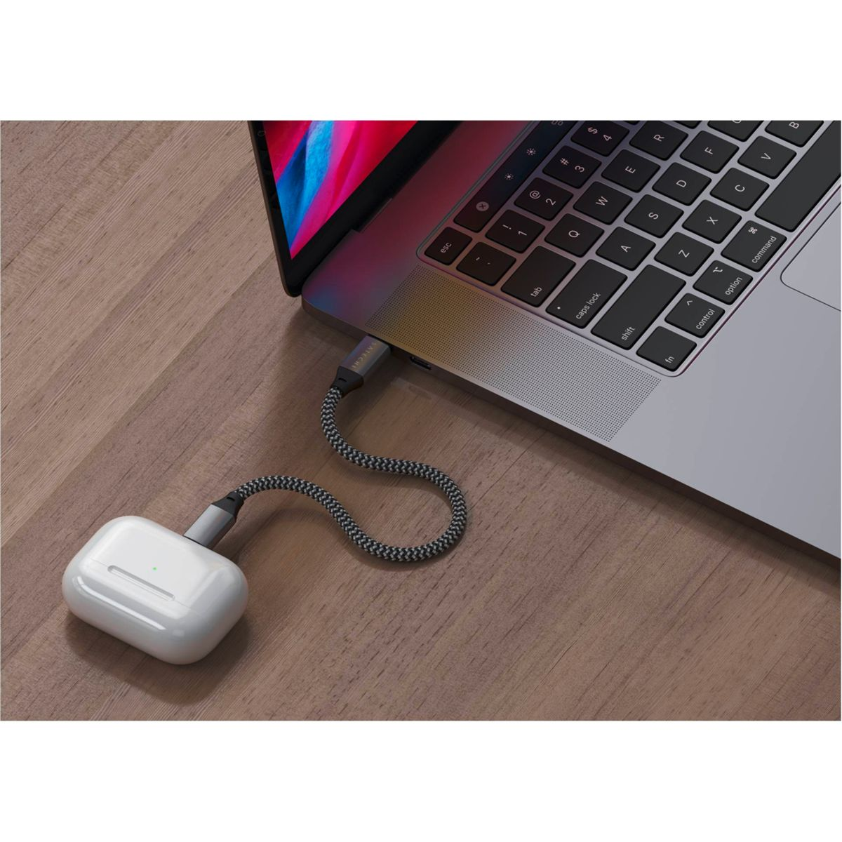 Un laptop, una custodia bianca per AirPods e un cavo di ricarica sono su un tavolo di legno.