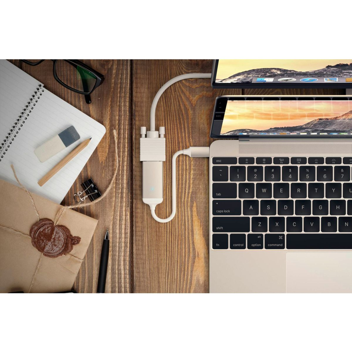 Laptop, der mit Displays und einem weißen Adapter auf einem Holztisch verbunden ist. Zubehör wie Brille und Notizbuch sind sichtbar.