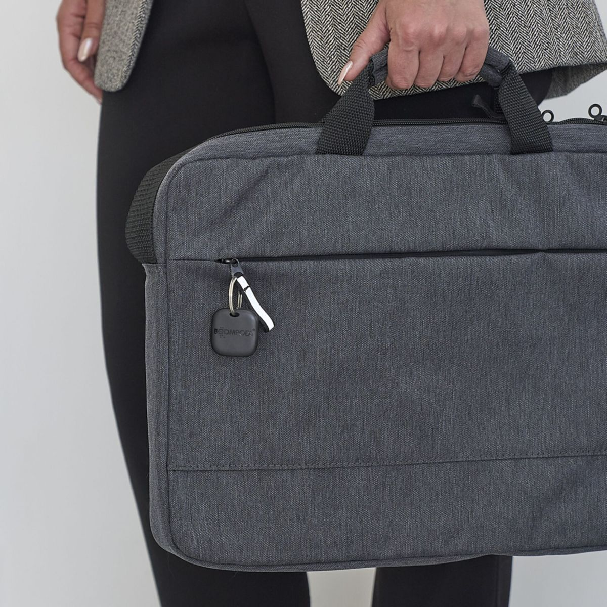 Osoba trzyma szarą torbę z dołączonym czarnym trackerem. Torba jest na jej ramieniu.