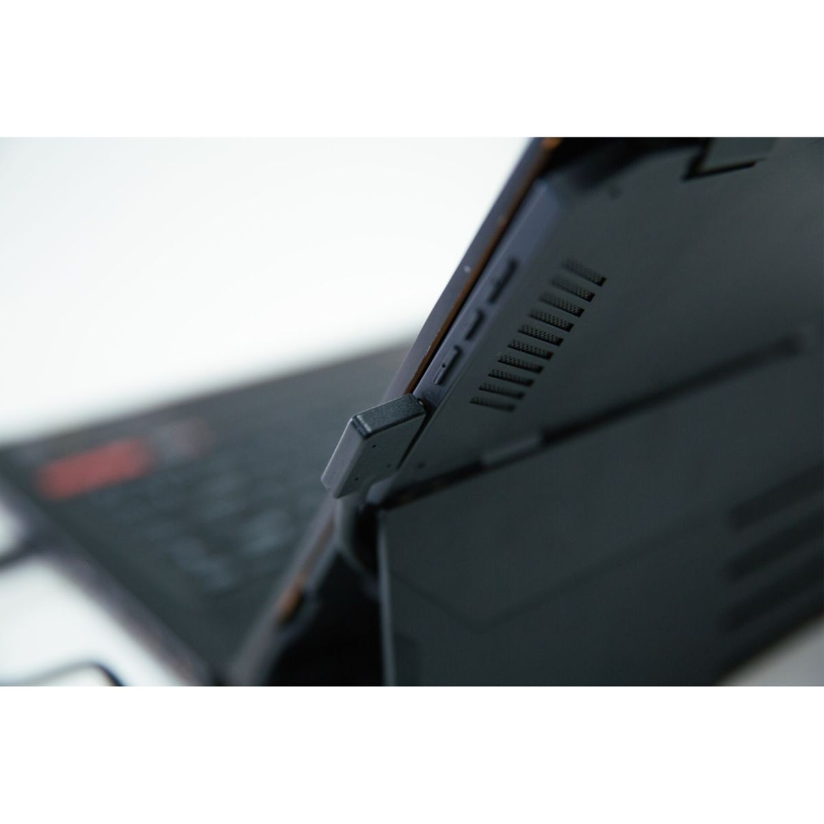 Czarny laptop z podniesionym ekranem, widok z boku. Laptop jest otwarty, spoczywa na białej powierzchni.