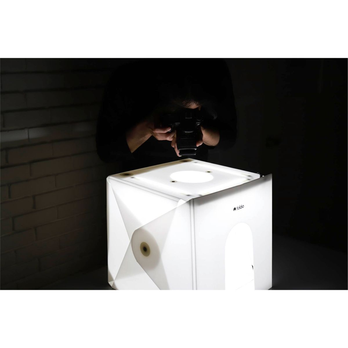 Persona tomando una foto de un cubo blanco con las luces encendidas. El cubo tiene un logo.