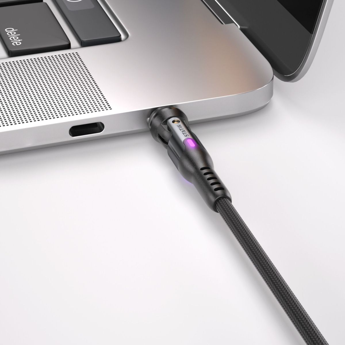 Ein schwarzes Ladekabel ist in einen Laptop eingesteckt. Das Kabel hat ein Licht. Grauer Hintergrund.