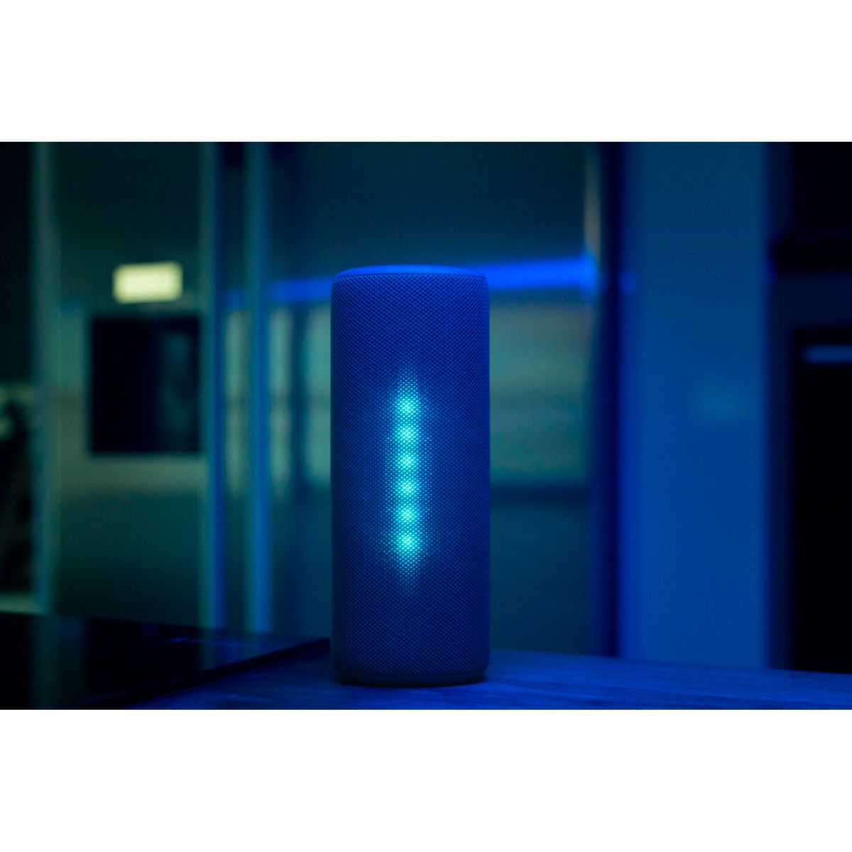 Un altoparlante blu che emette luce su una superficie di legno.