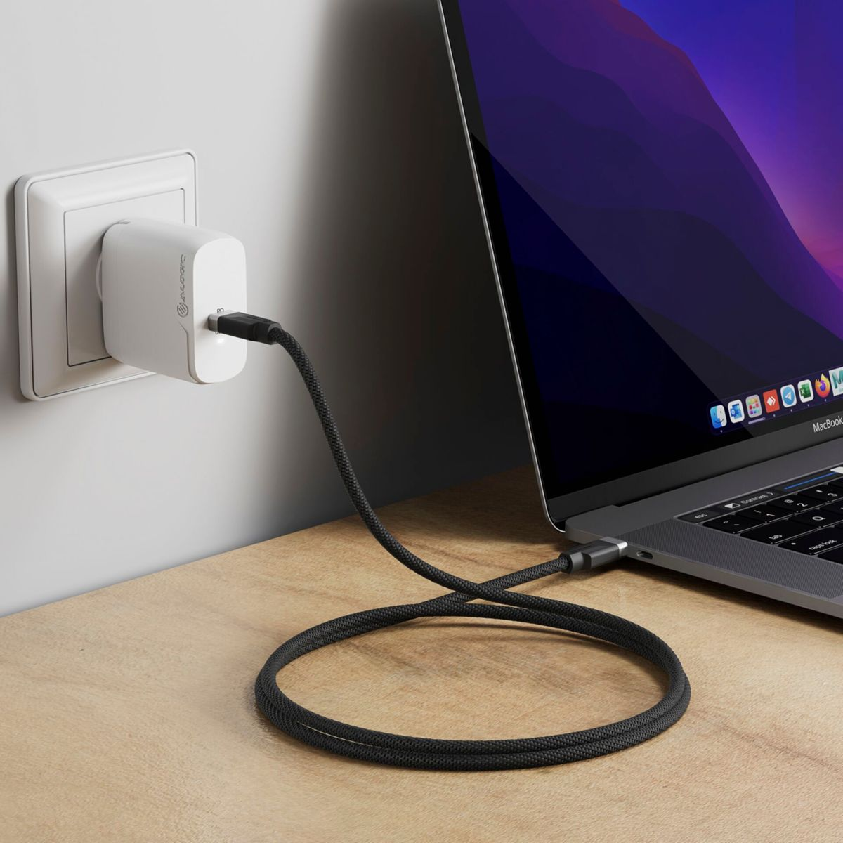 Un laptop collegato a un caricabatterie in una presa a muro, su una superficie di legno.
