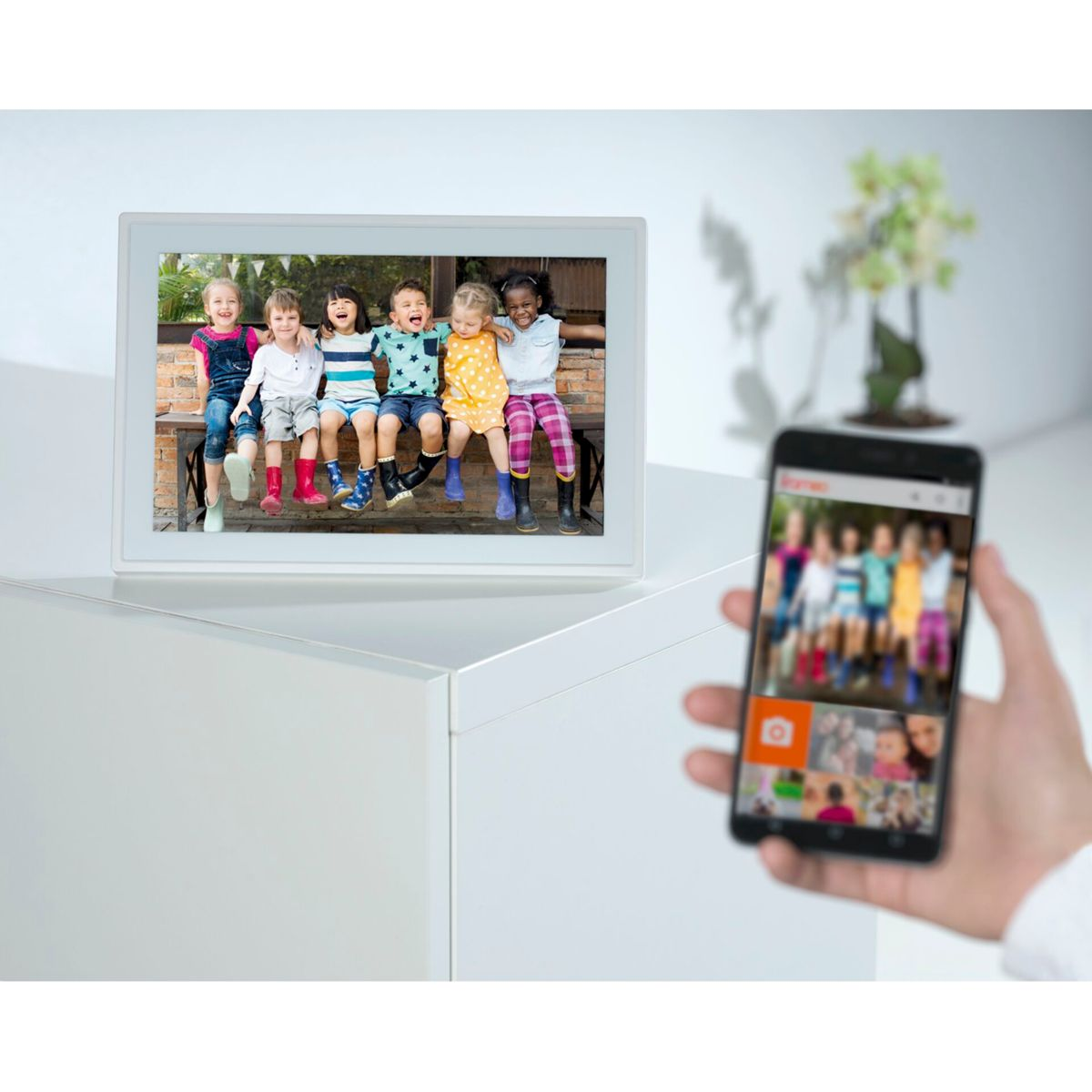 Ein digitaler Fotorahmen, der Kinder zeigt, mit einem Telefon, das ähnliche Bilder zeigt.