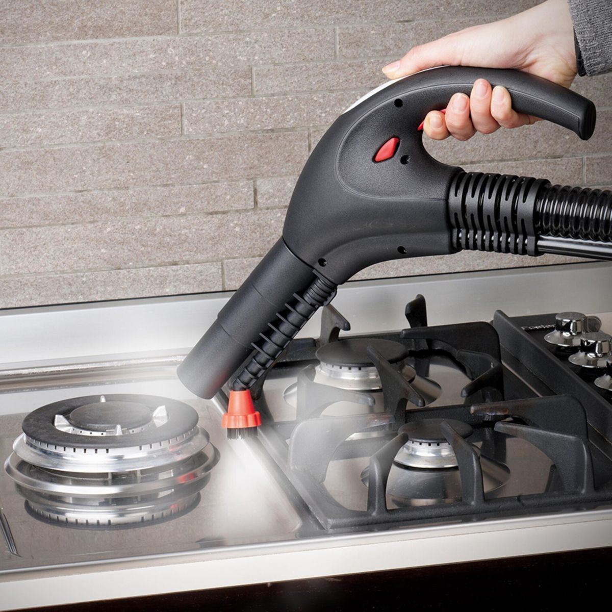 Ręka trzymająca czarny odkurzacz parowy nad kuchenką. Para unosi się z powierzchni kuchenki.