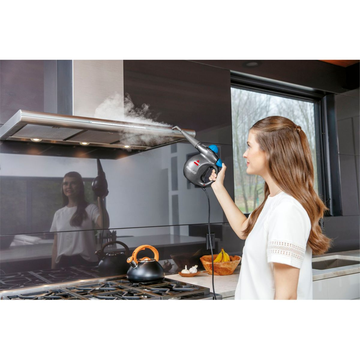 Kobieta czyści okap kuchenny za pomocą parownicy Bissell. Para wydobywa się.