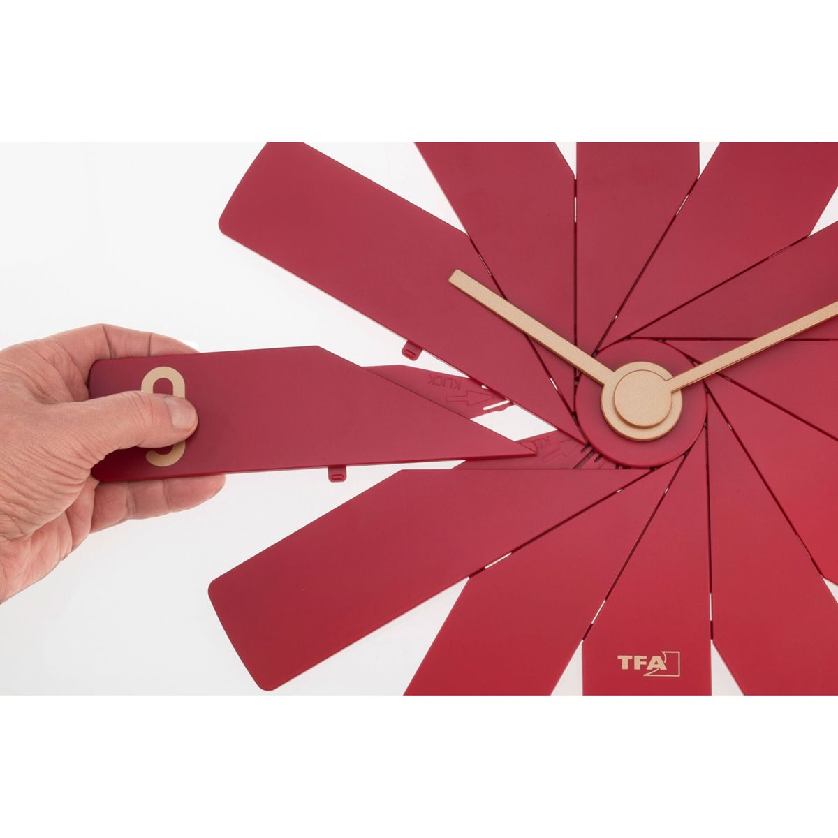 Die Hand einer Person legt die Zahl Acht auf eine rote Uhr. Die Uhr hat ein einzigartiges, geometrisches Design.