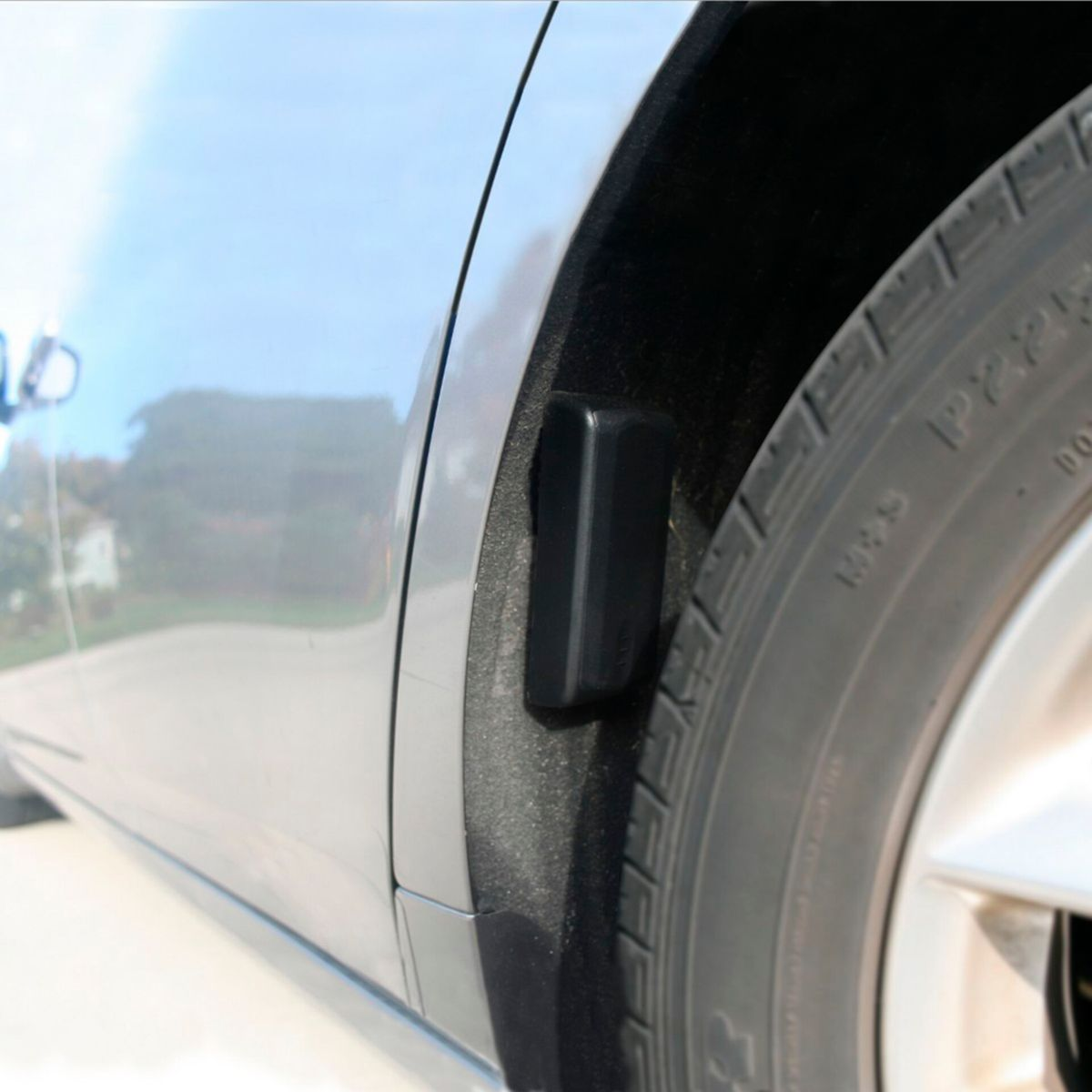 Un sensor negro está en el lateral de un neumático de coche. El coche es gris.
