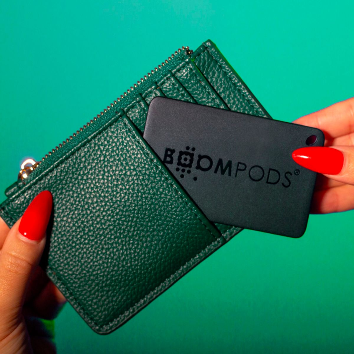Mani che tengono un portafoglio verde e una carta nera con il logo 'BOOMPODS'. Unghie rosse.