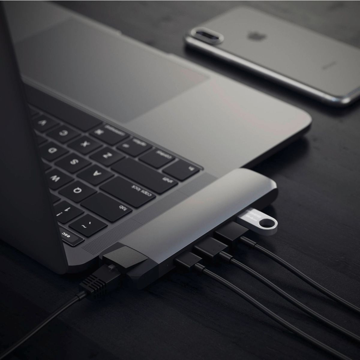 Laptop met aangesloten USB-hub, telefoon op de achtergrond.