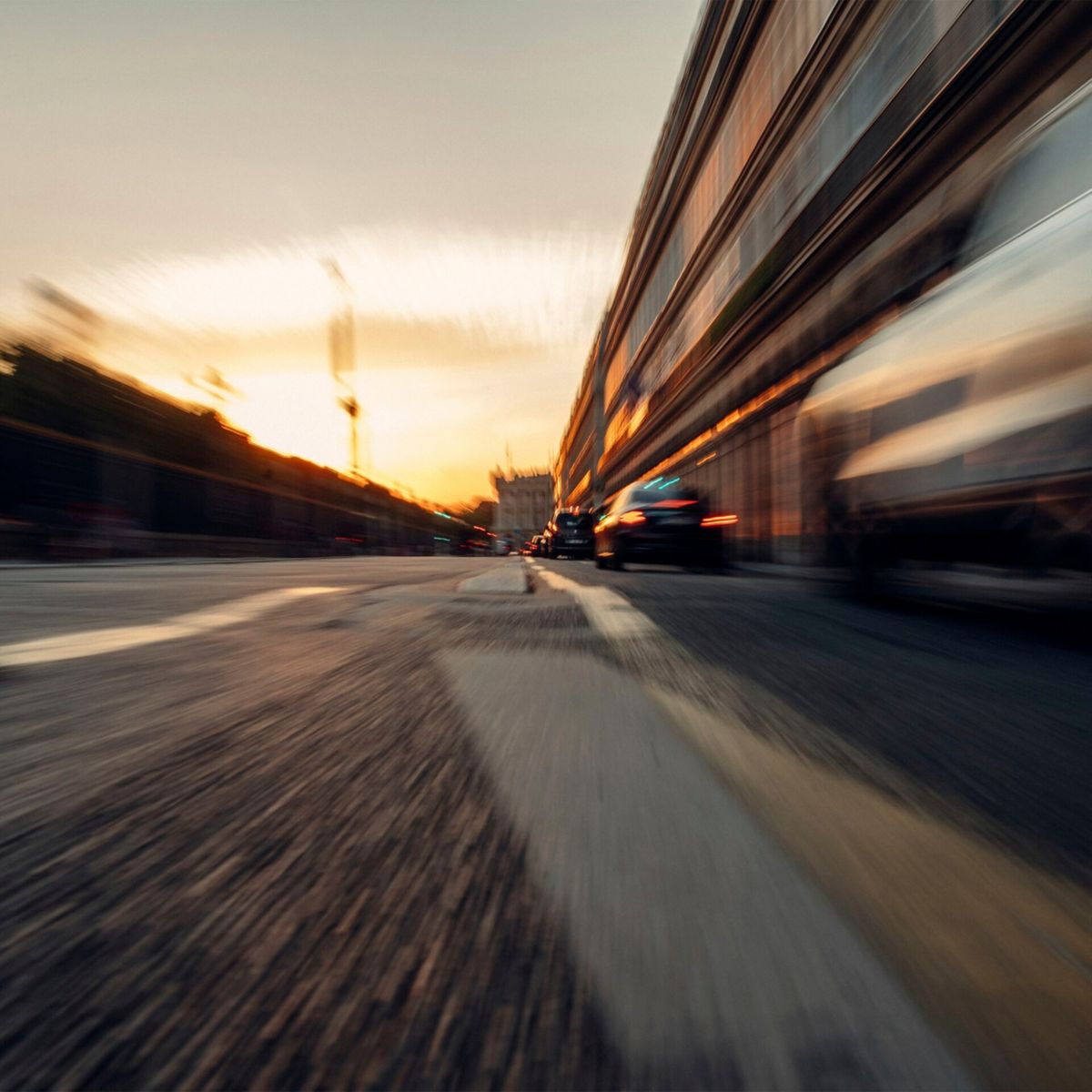 Straßenszene mit verschwommenen Autos und Sonnenuntergang im Hintergrund.