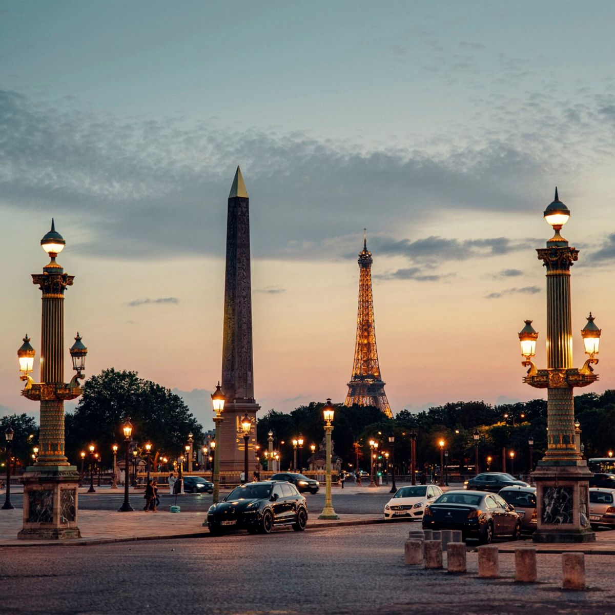 Paris in der Abenddämmerung, mit dem Eiffelturm und einem Obelisken im Hintergrund.
